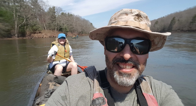 two people smile at the camera while paddling a canoe on an outward bound course